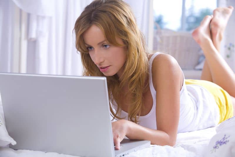 mujer acostada mirando laptop emocionada