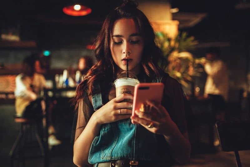 mujer bebiendo mientras ve celular